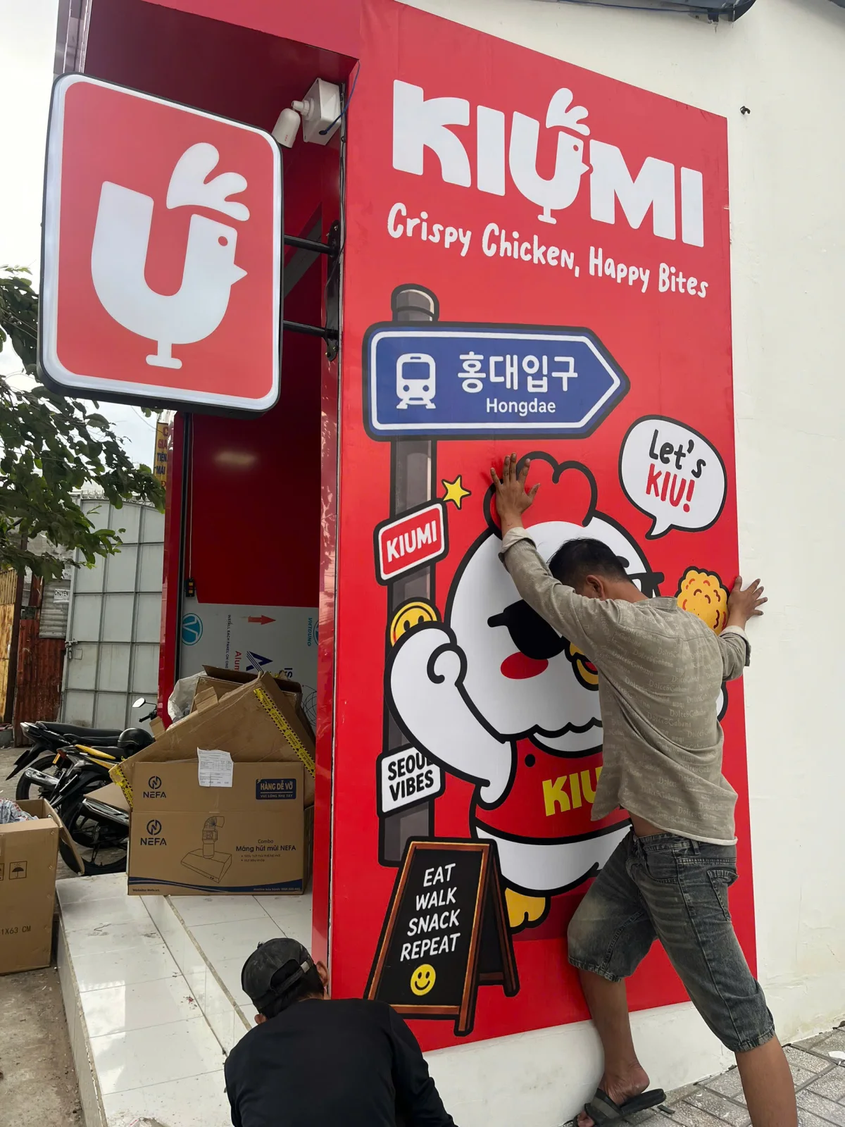 Nhân viên thi công đang căn chỉnh mảng đồ họa mascot và logo KIUMI trên tường ngoài