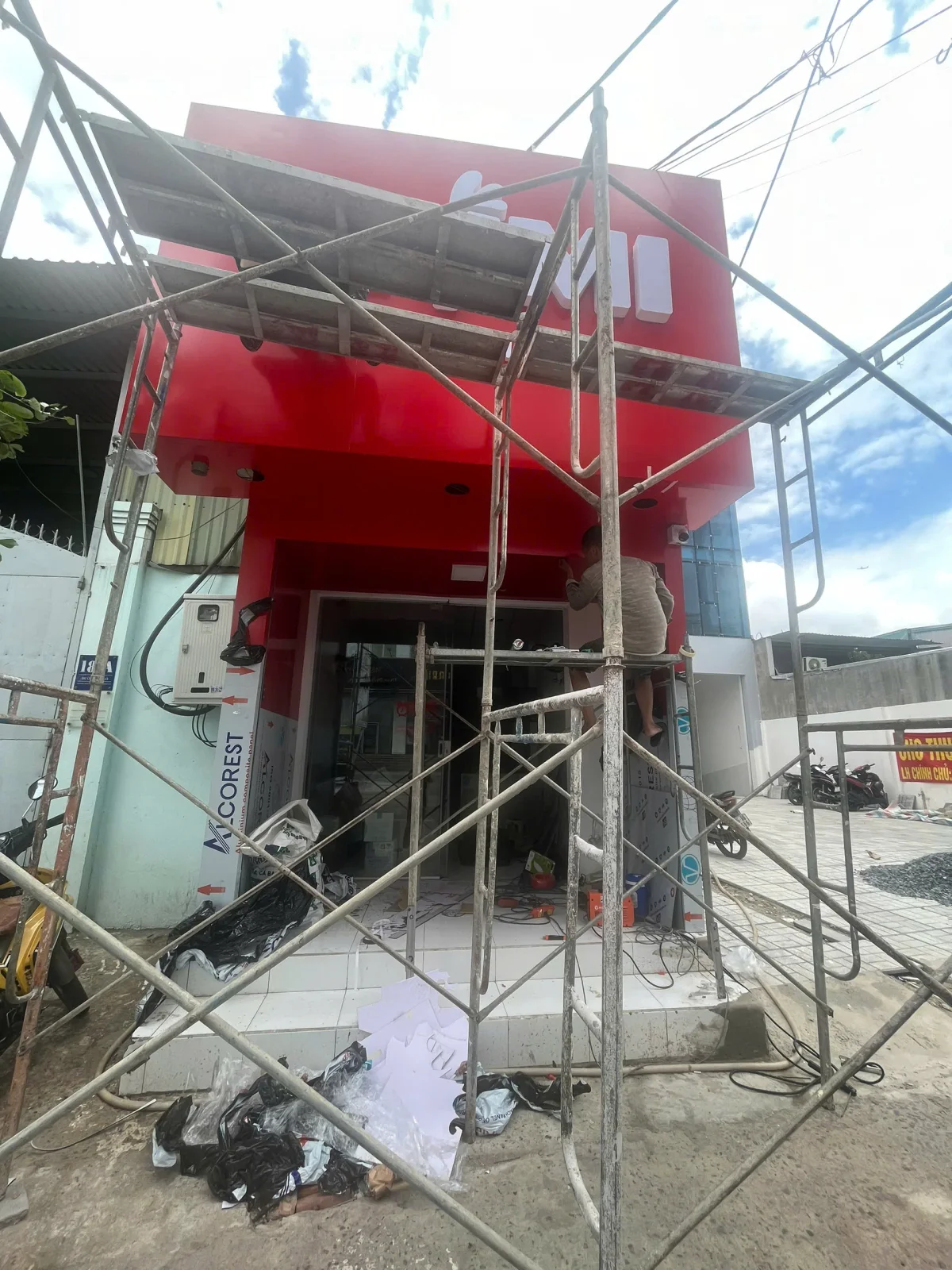 Mặt tiền KIUMI trong giai đoạn thi công với giàn giáo và hệ ốp màu đỏ